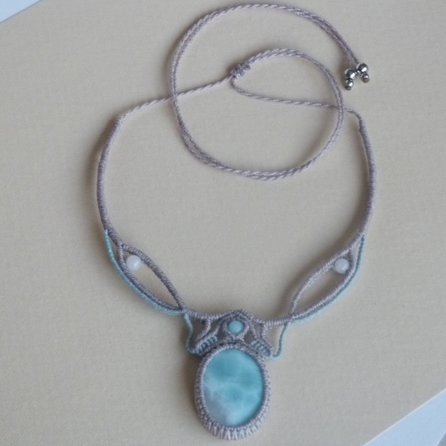 Collana in micro-macramè grigio tortora/blu smerigliato con al centro una gemma naturale nei toni tenui del bianco e dell'azzurro.