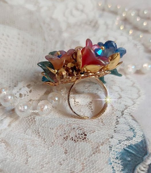 Bague Bel Air montée avec des fleurs lucites peintes à la main aux couleurs : Bleu, Rose, Rouge, Argent, Blanc avec feuilles ondulées Vert Cuivré à laquelle s’ajoute perles Dorées en Verre