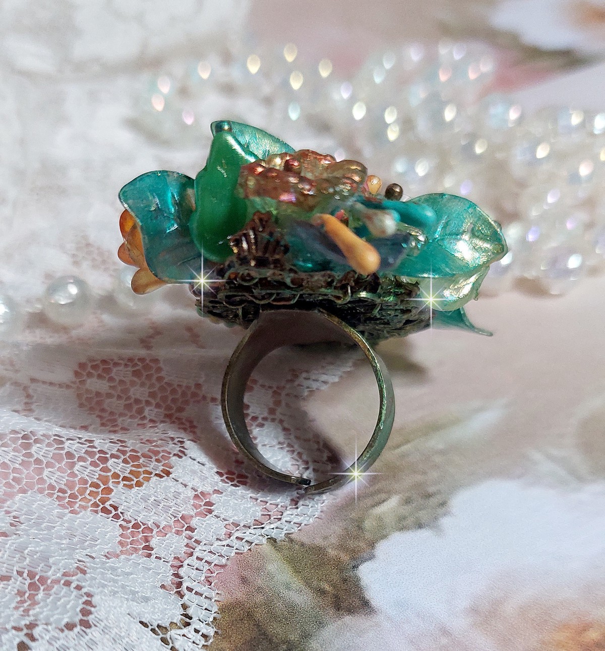 Bague Patiflo d’une composition florale créée avec des cristaux, fleurs en Résine, perles, clochettes, pensées, boutons de rose en Verre, estampes et coupelles. Le tout est monté sur une bague estampe