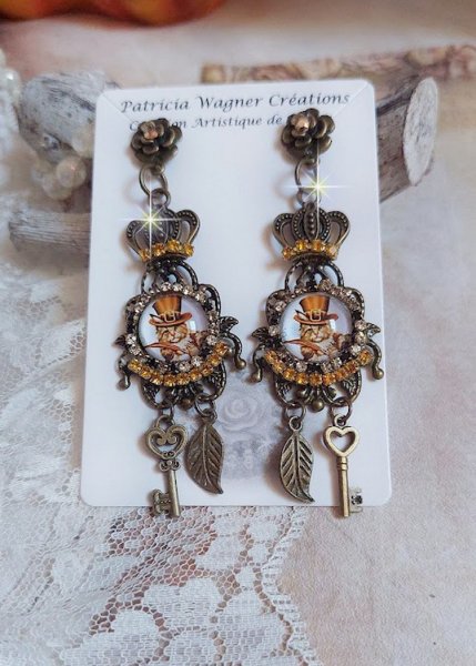 BO Chatibo Steampunk mont&eacute;es avec cabochons ronds en verre repr&eacute;sentant un chat chapeaut&eacute; Haute de Forme Orange. Strass&eacute;es avec une couronne, breloques cl&eacute;s et feuilles. Mont&eacute;es sur clips Bronze