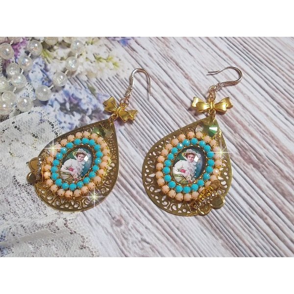 BO Mademoiselle Noellia avec des cabochons ovales repr&eacute;sentant une femme avec un chapeau et un n&oelig;ud blanc &agrave; laquelle s&rsquo;ajoute des cristaux, cha&icirc;nes strass P&ecirc;che et Turquoise sur crochets en plaqu&eacute; Or