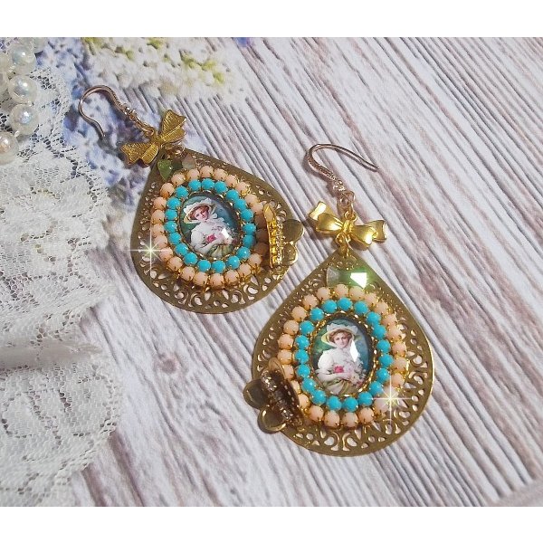 BO Mademoiselle Noellia avec des cabochons ovales repr&eacute;sentant une femme avec un chapeau et un n&oelig;ud blanc &agrave; laquelle s&rsquo;ajoute des cristaux, cha&icirc;nes strass P&ecirc;che et Turquoise sur crochets en plaqu&eacute; Or