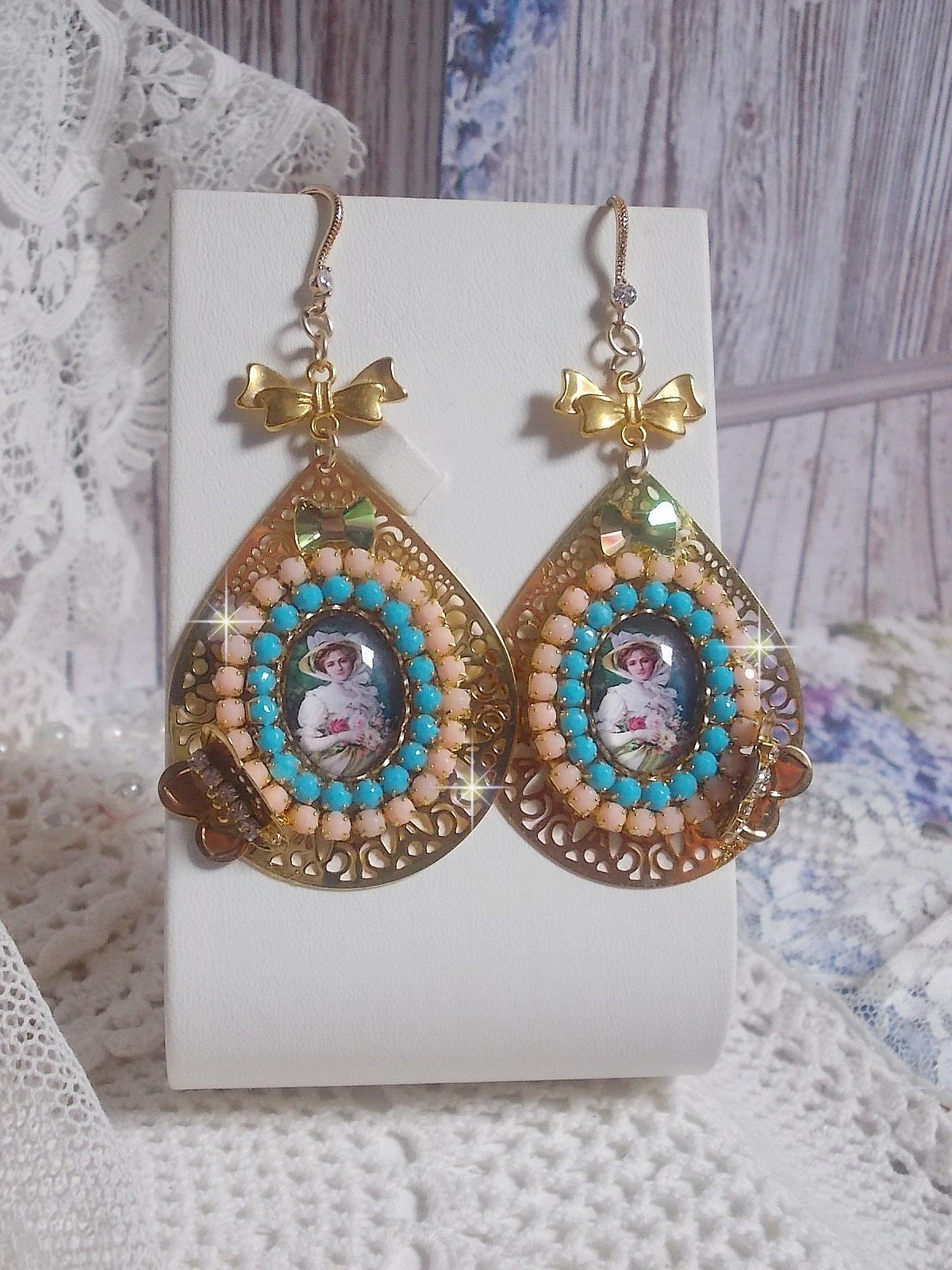 BO Mademoiselle Noellia avec des cabochons ovales repr&eacute;sentant une femme avec un chapeau et un n&oelig;ud blanc &agrave; laquelle s&rsquo;ajoute des cristaux, cha&icirc;nes strass P&ecirc;che et Turquoise sur crochets en plaqu&eacute; Or