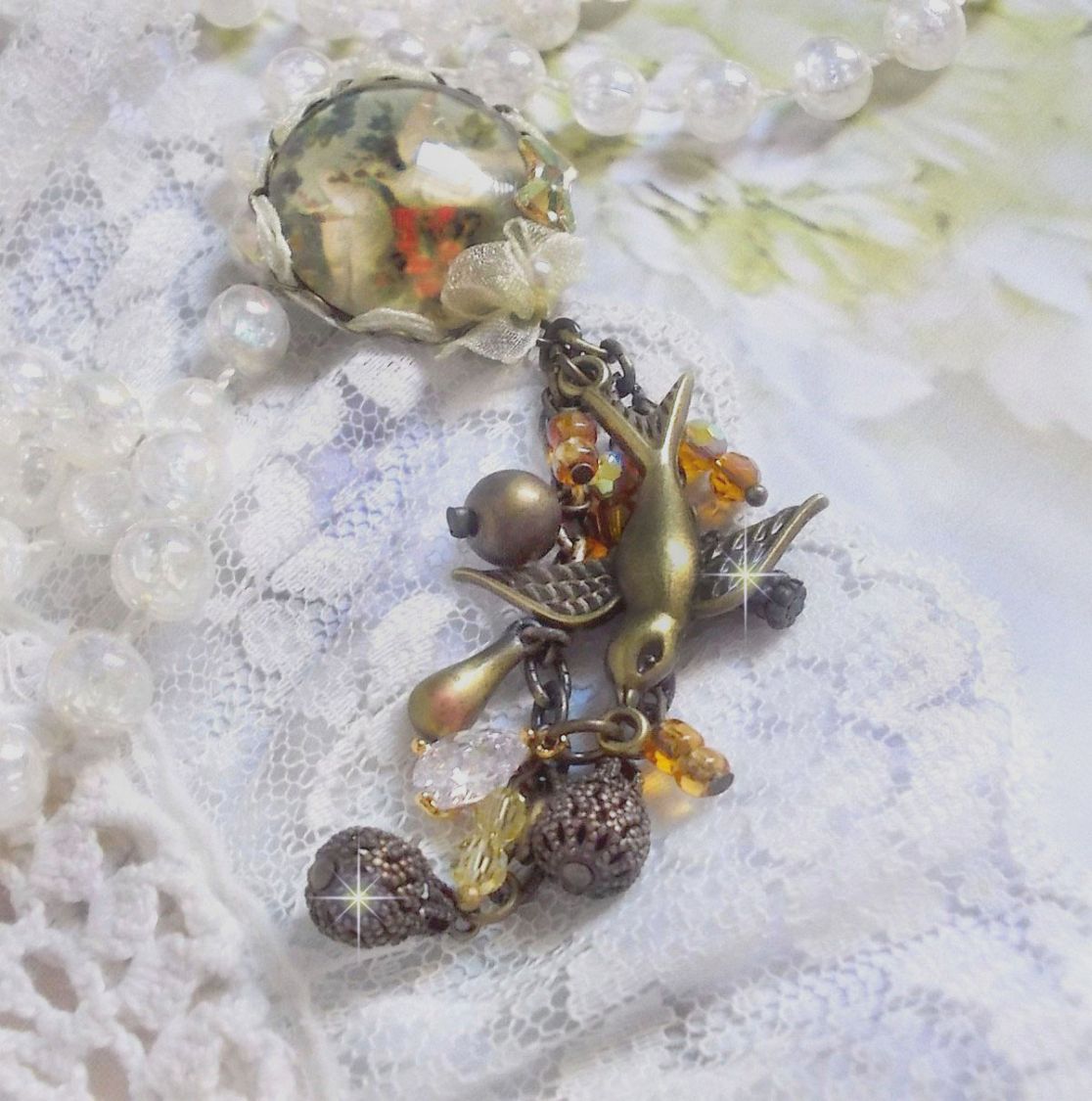 Broche Colombes aux plumages blancs avec des breloques filigranées gouttes et lisses, perles rondes et nœud en cristal, ruban organza crème, pendentif plaqué or avec un zircon sur une broche en métal