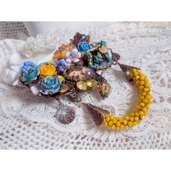 Broche Eclats P&eacute;tillants d&rsquo;inspiration Baroque, orn&eacute;e de fleurs en r&eacute;sine autour d&rsquo;un cabochon strass&eacute;s et perl&eacute;s sur estampes, cristaux, breloques, perle cloisonn&eacute;e, perles jaunes en verre et roses. 