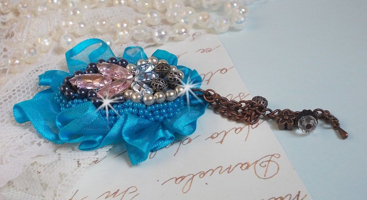 La spilla Belle Epoque Haute-Couture è ricamata con cristalli Swarovski, perle rotonde, ciondoli, nastri e perline.