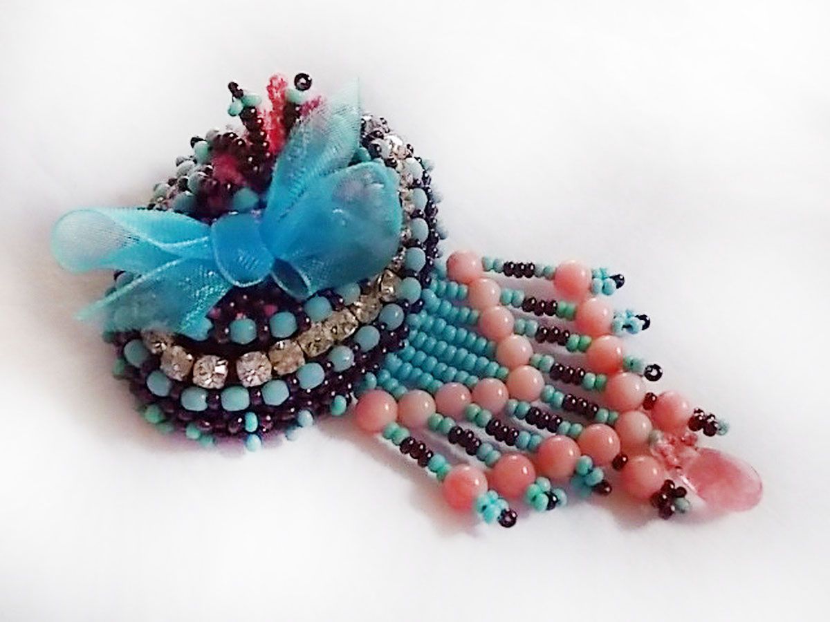 Spilla a forma di naiade ricamata con perle di pietra (turchese e corallo), cristalli, pelle di vacchetta e perle di seme