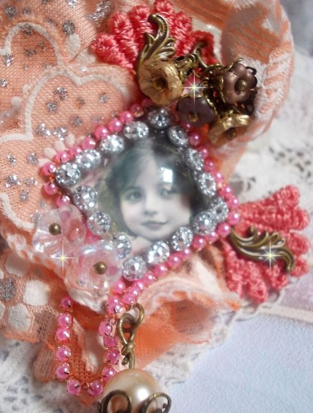 Spilla a forma di rosa rustica creata con un cabochon raffigurante una ragazza sorridente, strass arancione e pizzo rosa, cristalli, perline di vetro e accessori vari.