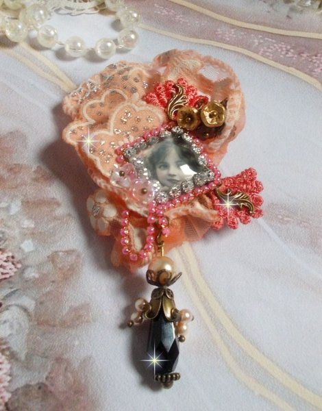 Spilla a forma di rosa rustica creata con un cabochon raffigurante una ragazza sorridente, strass arancione e pizzo rosa, cristalli, perline di vetro e accessori vari.