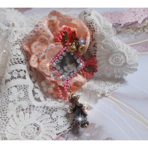 Spilla a forma di rosa rustica creata con un cabochon raffigurante una ragazza sorridente, strass arancione e pizzo rosa, cristalli, perline di vetro e accessori vari.