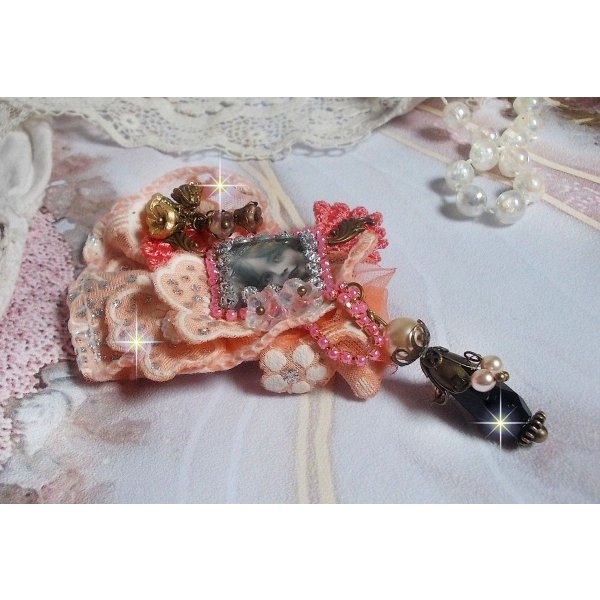 Spilla a forma di rosa rustica creata con un cabochon raffigurante una ragazza sorridente, strass arancione e pizzo rosa, cristalli, perline di vetro e accessori vari.