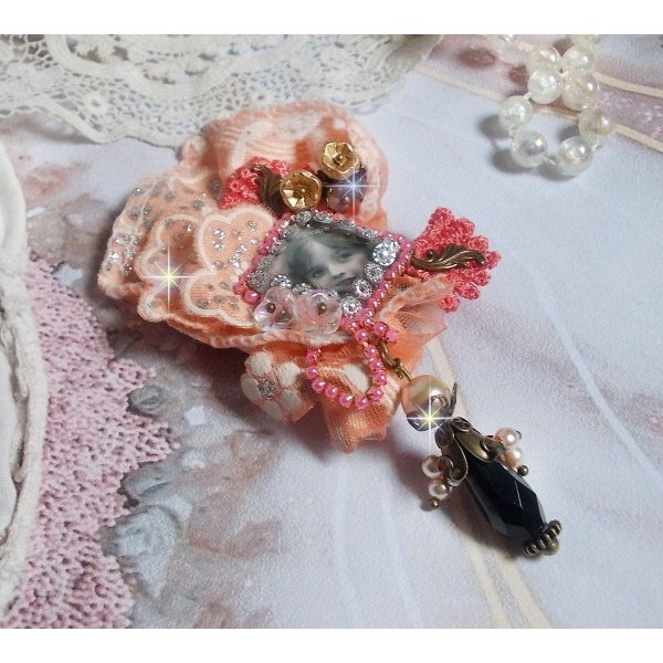 Spilla a forma di rosa rustica creata con un cabochon raffigurante una ragazza sorridente, strass arancione e pizzo rosa, cristalli, perline di vetro e accessori vari.