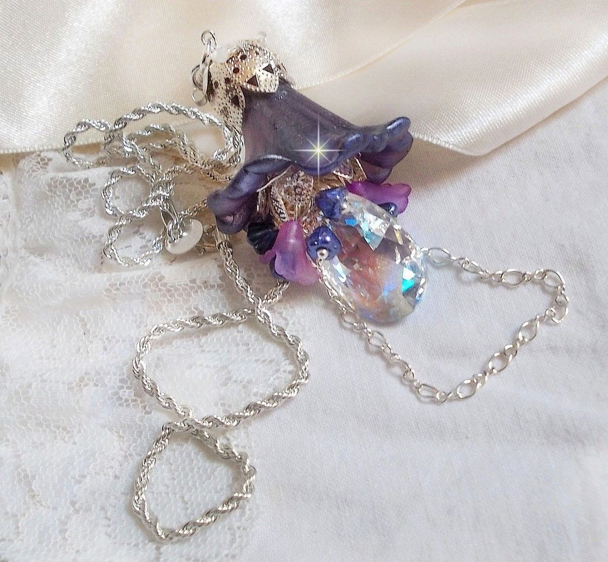 Pendentif Eclat de Cristal monté avec une goutte en Cristal, fleurs en Verre, fleurs lucites dont une plus grande peinte à la main avec paillettes Argentées. Une composition florale