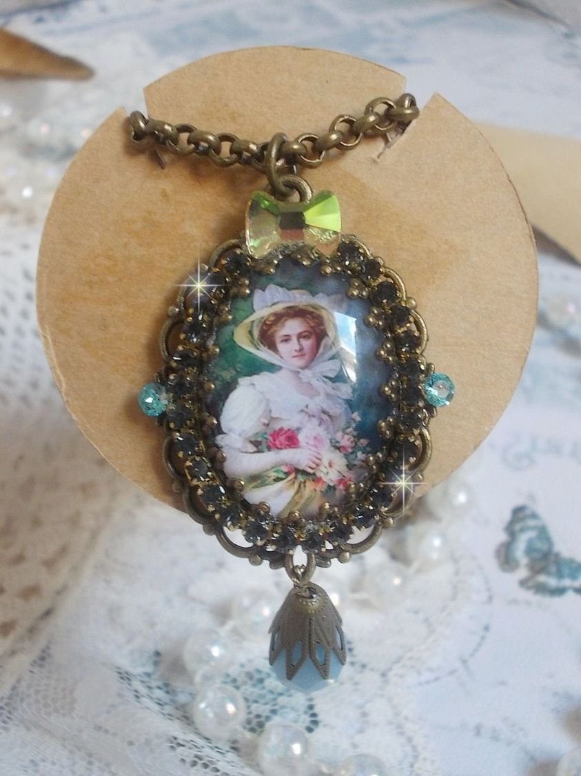 Pendentif Douce Dame créé avec un cabochon représentant une femme au chapeau blanc orné de cristaux, des accessoires de couleur Bronze et un jade teinté bleu 